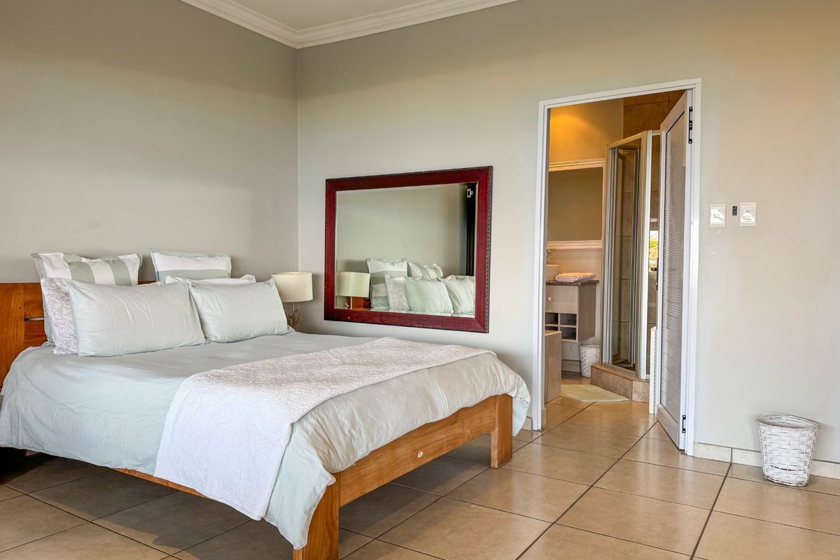 A spacious bedroom featuring neutral wall tones, tiled flooring, and an en-suite bathroom accessible through a doorway.