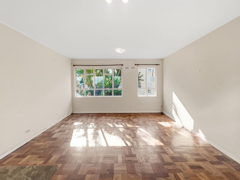 A bright, empty living room featuring classic parquet flooring and large windows that provide ample natural light.