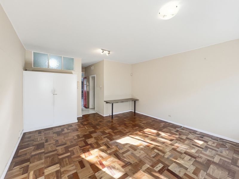 A spacious, empty living area featuring classic parquet flooring, neutral walls, and a built-in storage cupboard.