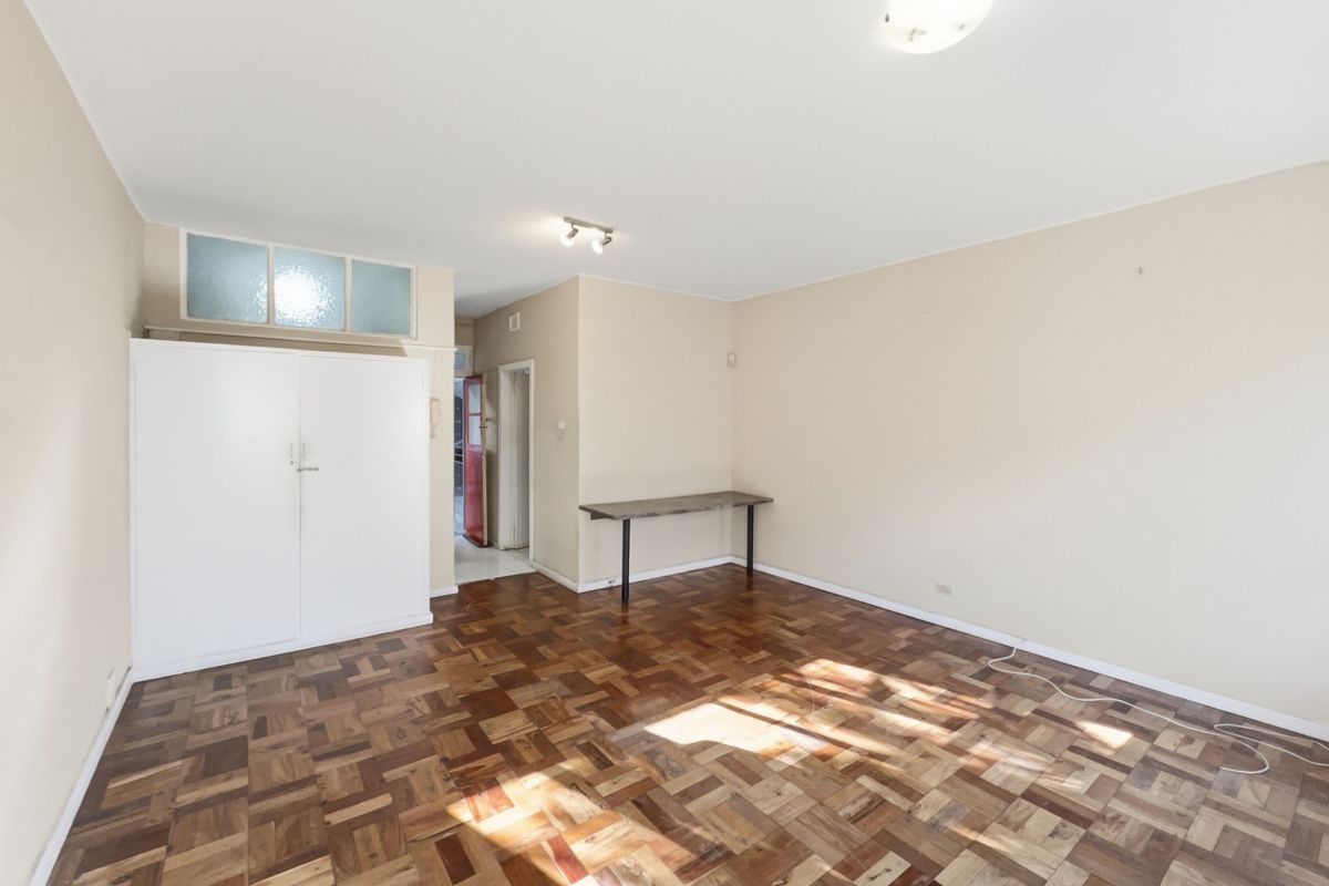 A spacious, empty living area featuring classic parquet flooring, neutral walls, and a built-in storage cupboard.