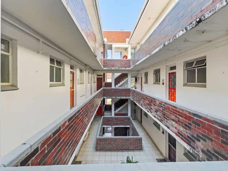 An open-air central courtyard and walkway area featuring brick facade detailing, tiled flooring, and access to multiple residential units.