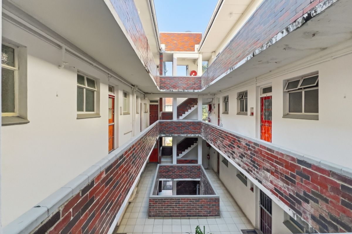 An open-air central courtyard and walkway area featuring brick facade detailing, tiled flooring, and access to multiple residential units.