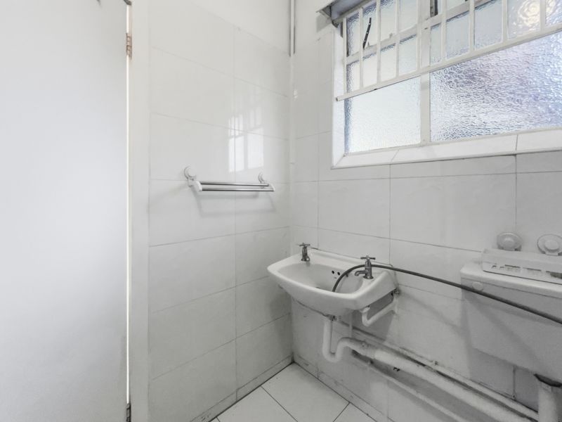 A compact, functional bathroom featuring white tiled walls, a wall-mounted basin, and an obscured glass window for privacy.