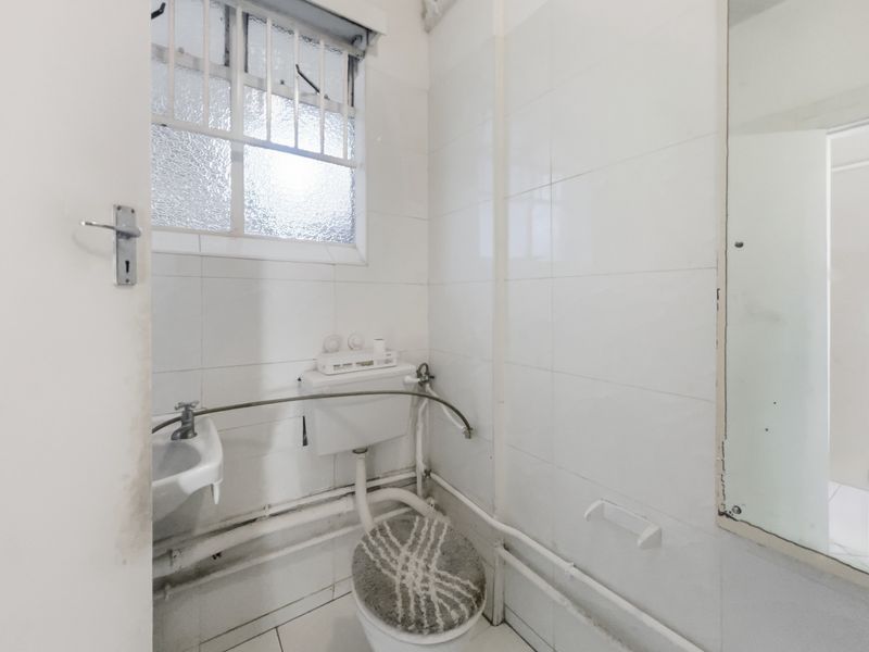 A compact, functional bathroom featuring tiled walls, a wall-mounted basin, and a toilet with exposed plumbing.