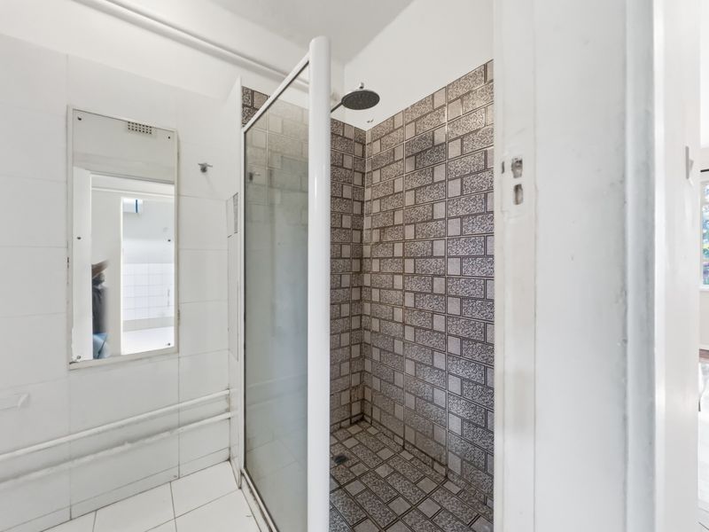 A functional bathroom featuring a walk-in shower with patterned tiling and a wall-mounted mirror, requiring cosmetic updates to improve its overall aesthetic.