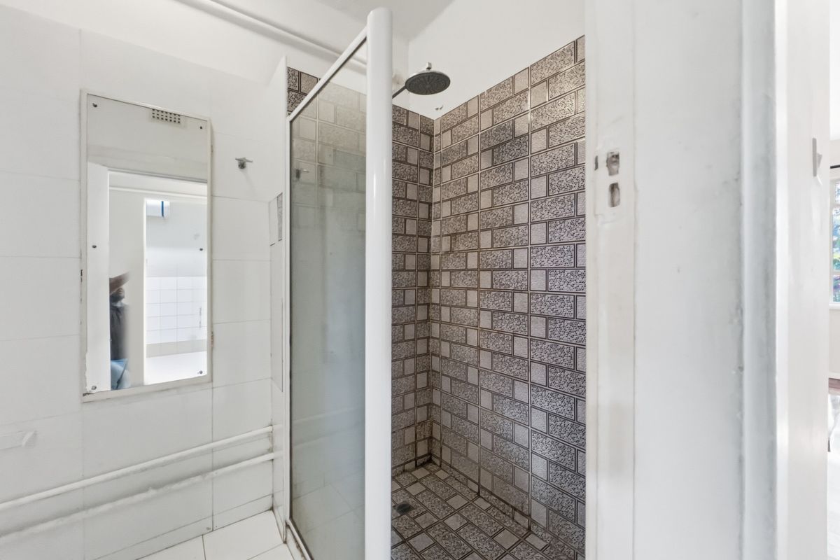 A functional bathroom featuring a walk-in shower with patterned tiling and a wall-mounted mirror, requiring cosmetic updates to improve its overall aesthetic.