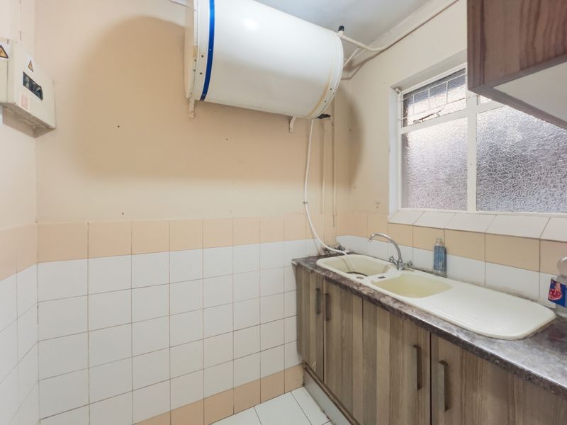 A functional laundry area featuring a double basin sink, laminate countertop, base cabinetry, and an electric water heater mounted on the wall.