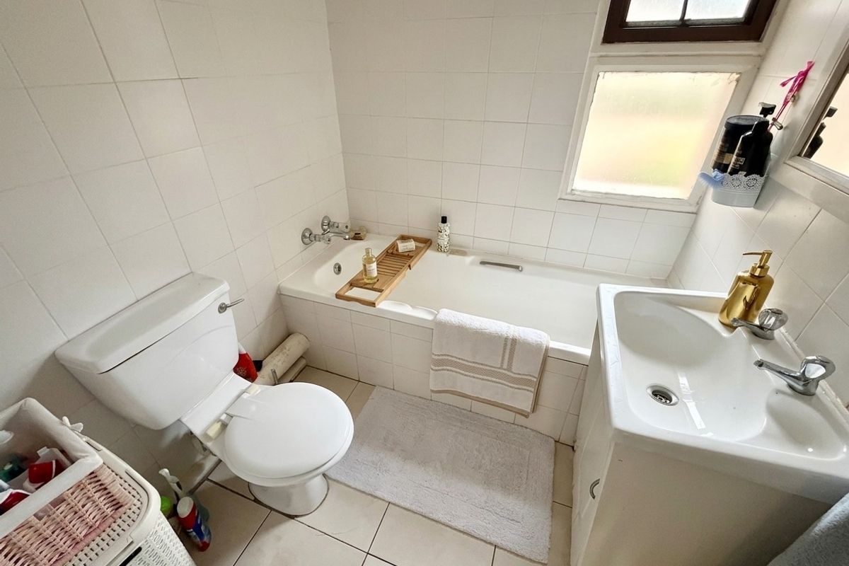 A functional bathroom featuring a built-in bathtub, vanity basin, and toilet, finished with white ceramic wall and floor tiles.