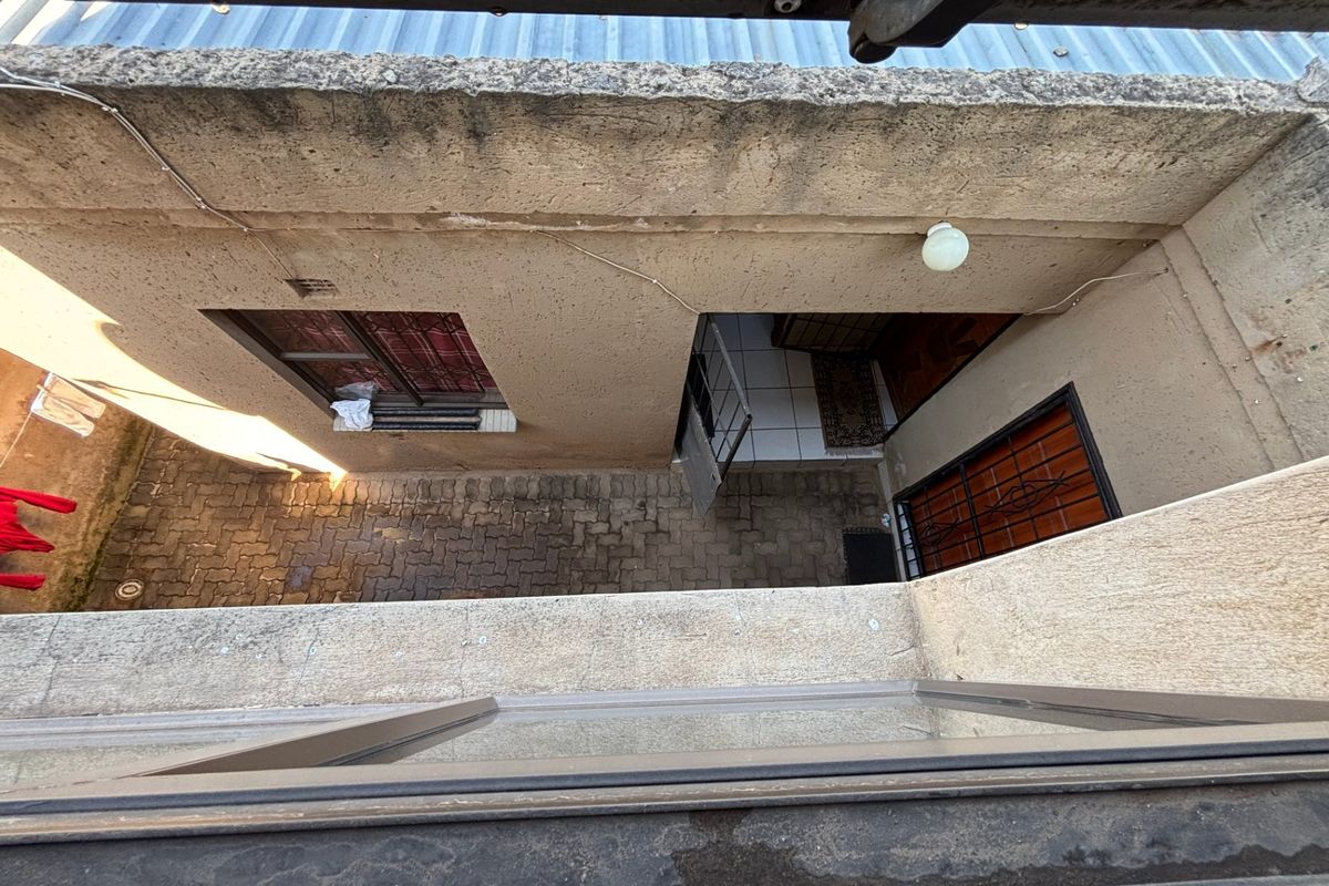 An elevated view looking down into a paved courtyard area between building sections, featuring exterior masonry walls and security-grille windows.