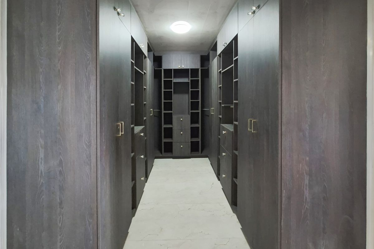 A walk-in closet featuring extensive dark wood built-in cabinetry with integrated shelving, drawers, and light-colored tiled flooring.