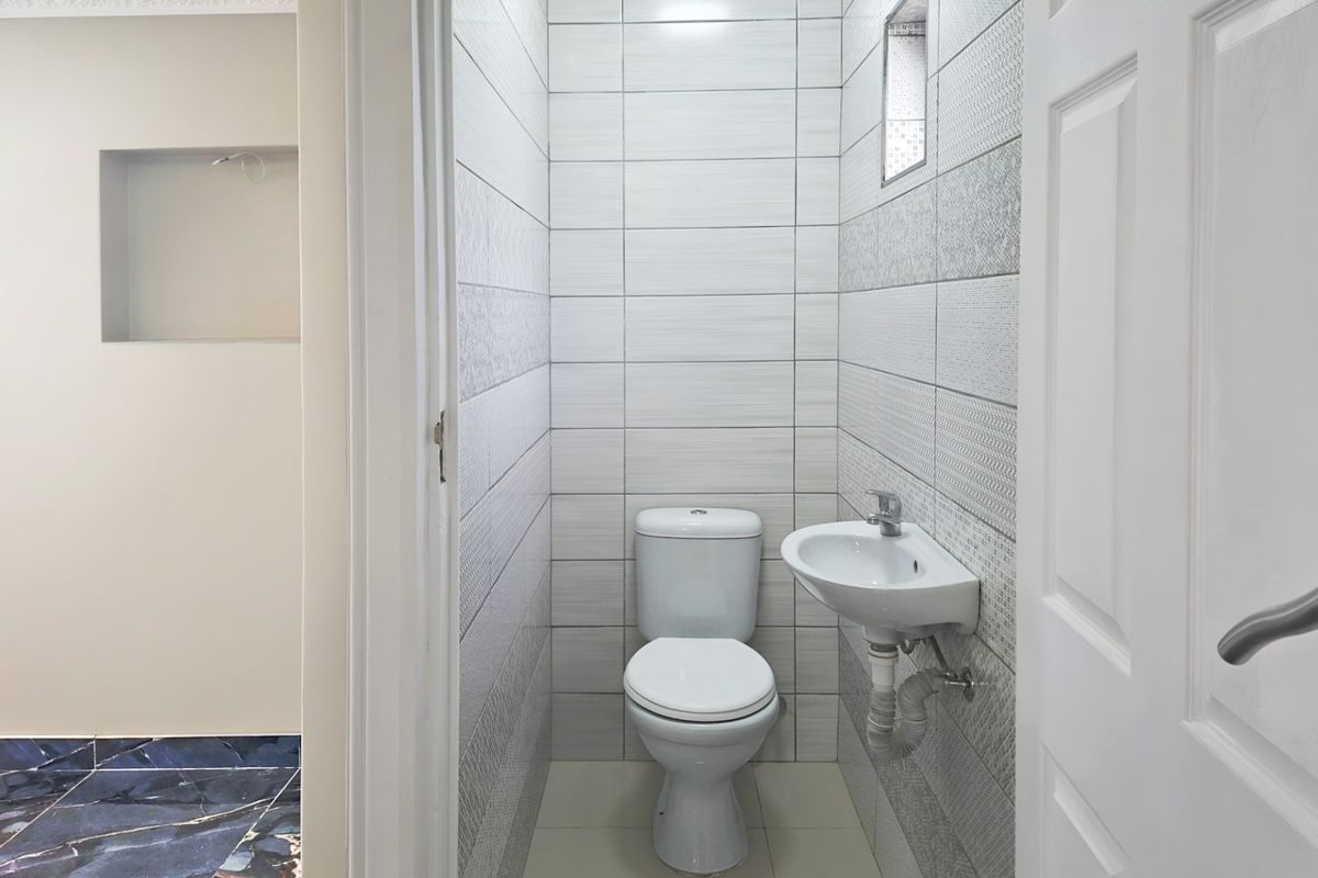 A compact, modern bathroom featuring tiled walls, a wall-mounted basin, and a standard toilet, with a clean and functional layout.
