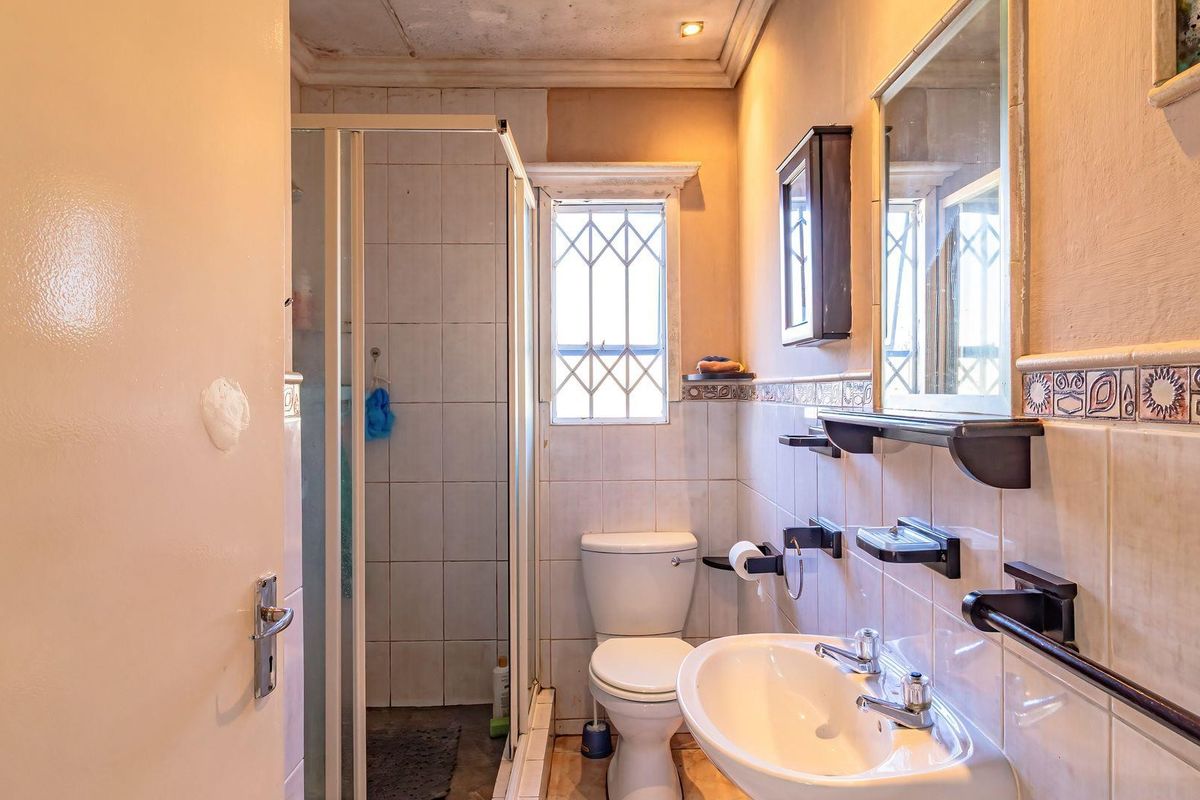 A compact bathroom featuring a corner shower enclosure, pedestal basin, and toilet, with dated finishes and visible signs of wear on the ceiling and walls.