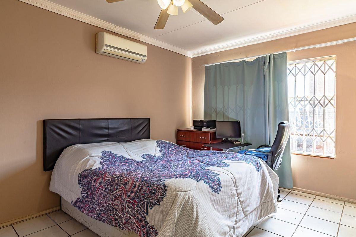 A bedroom featuring tiled flooring, a ceiling fan, and a wall-mounted air conditioning unit, with security bars installed on the window.