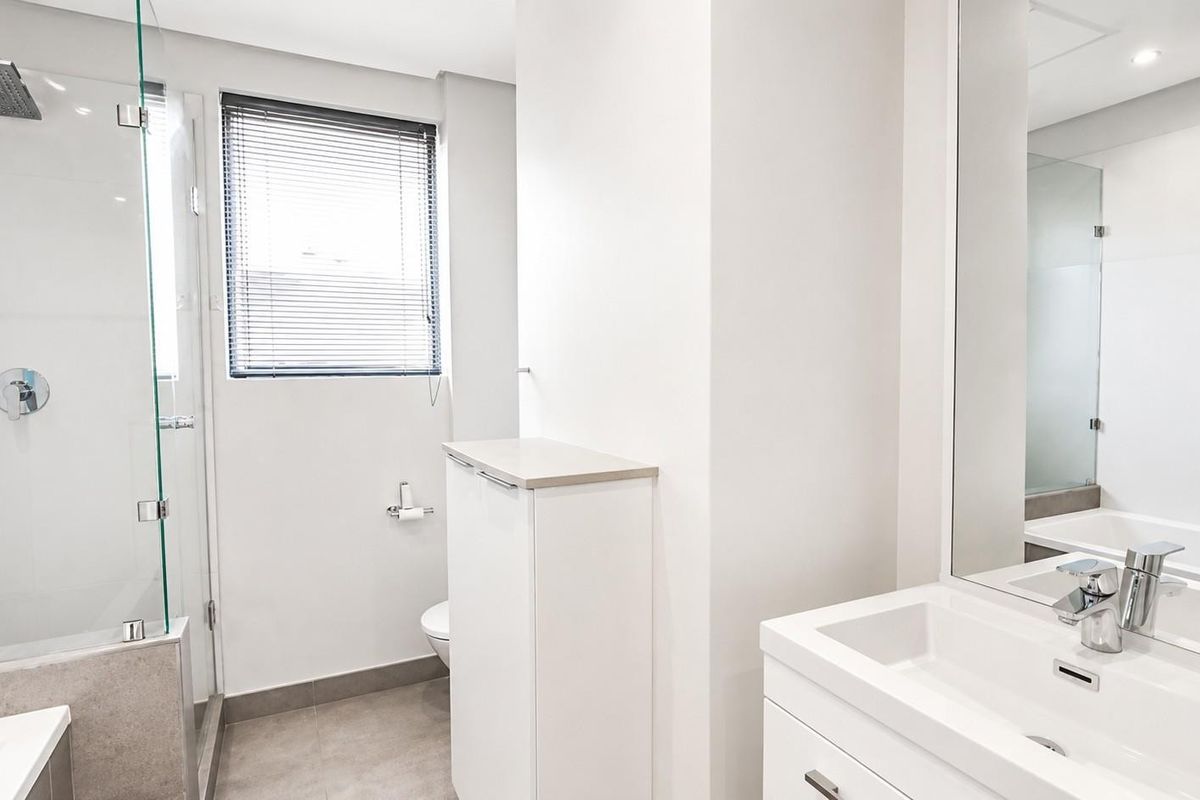 Modern bathroom featuring a glass-enclosed shower with rain head, vanity with basin, large mirror, and neutral tiled finishes.