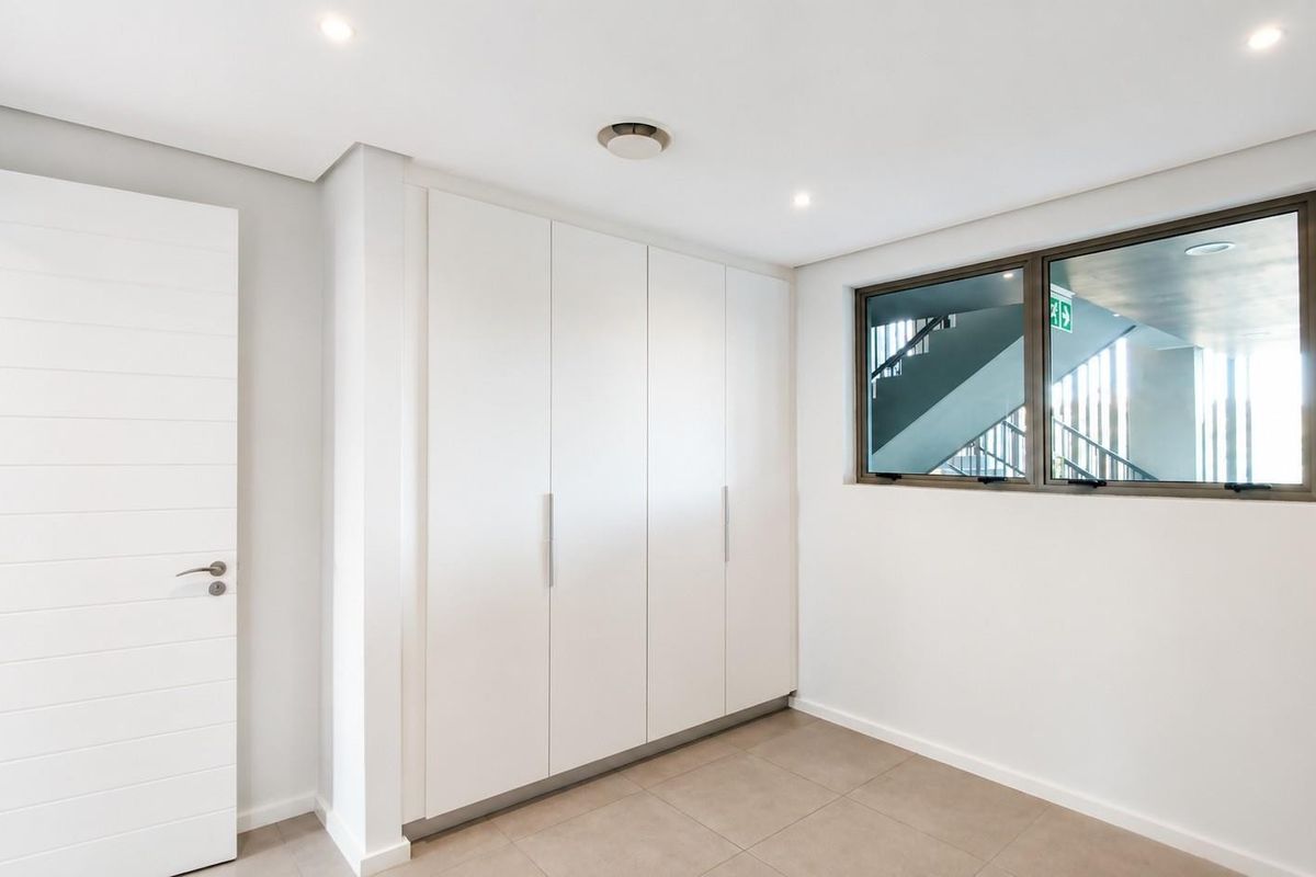 A bright, modern bedroom featuring neutral tiled flooring, ample built-in cupboard storage, and recessed lighting, offering a clean and versatile living space.