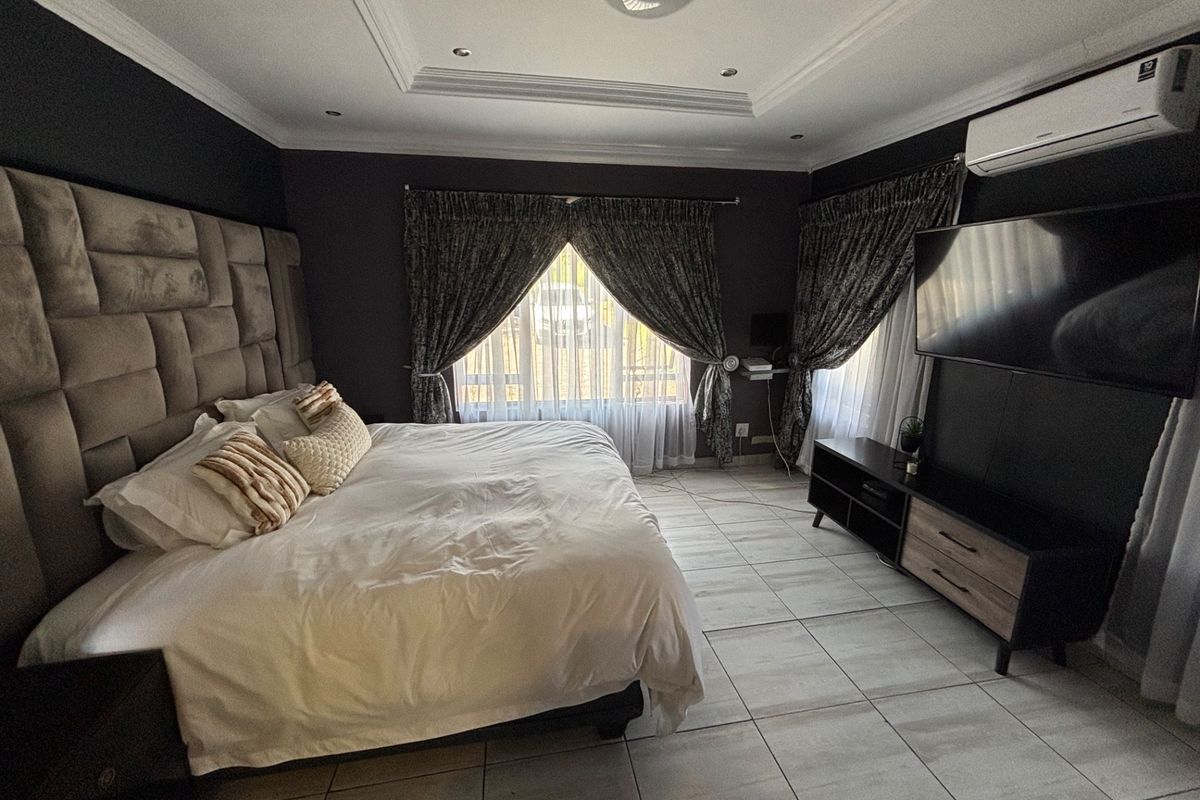 A well-maintained bedroom featuring tiled flooring, recessed ceiling detail, and a wall-mounted air conditioning unit.