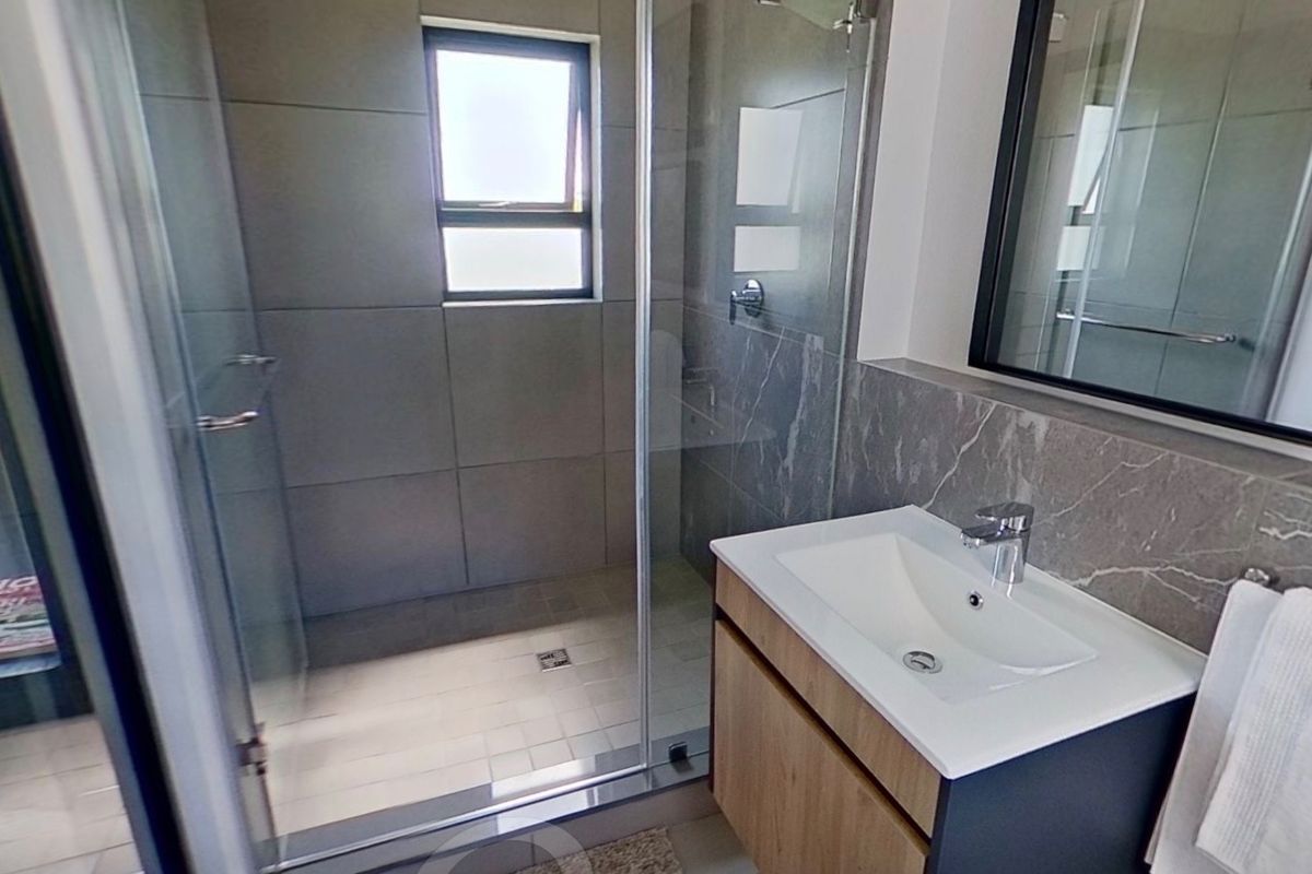 Modern bathroom featuring a glass-enclosed shower, contemporary vanity with basin, and stylish grey wall tiling.