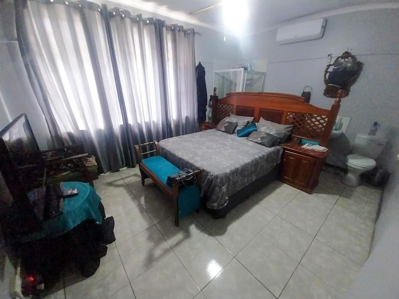 Spacious bedroom featuring ceramic floor tiles, a wall-mounted split-system air conditioner, and an integrated en-suite toilet facility.