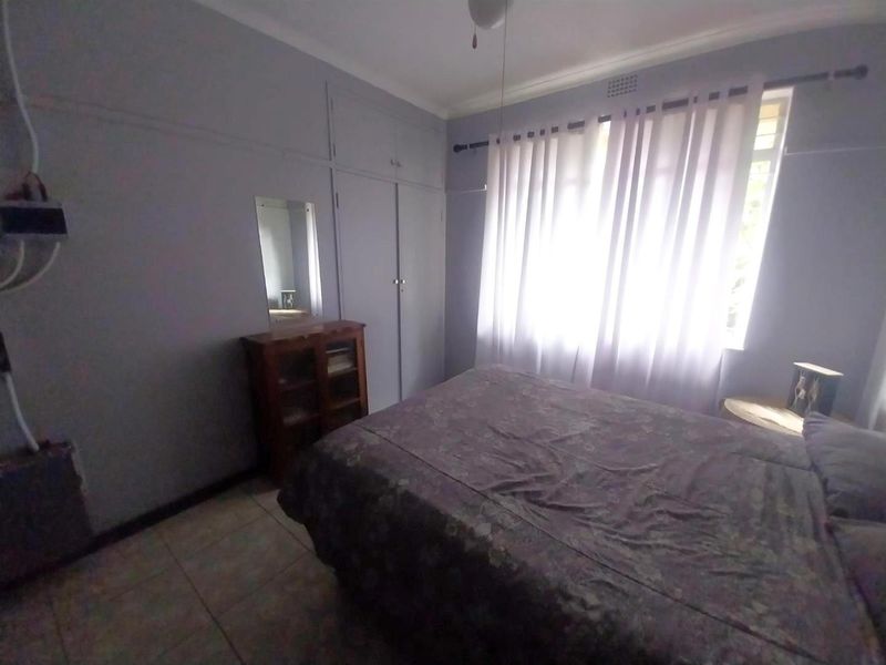 A bedroom featuring built-in cupboards, tiled flooring, and natural light through a window with curtains.