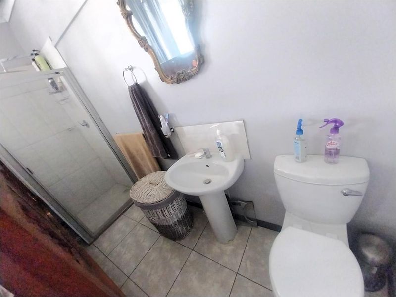 A functional bathroom featuring a pedestal basin, a glass-enclosed shower, and a standard toilet with tiled flooring.