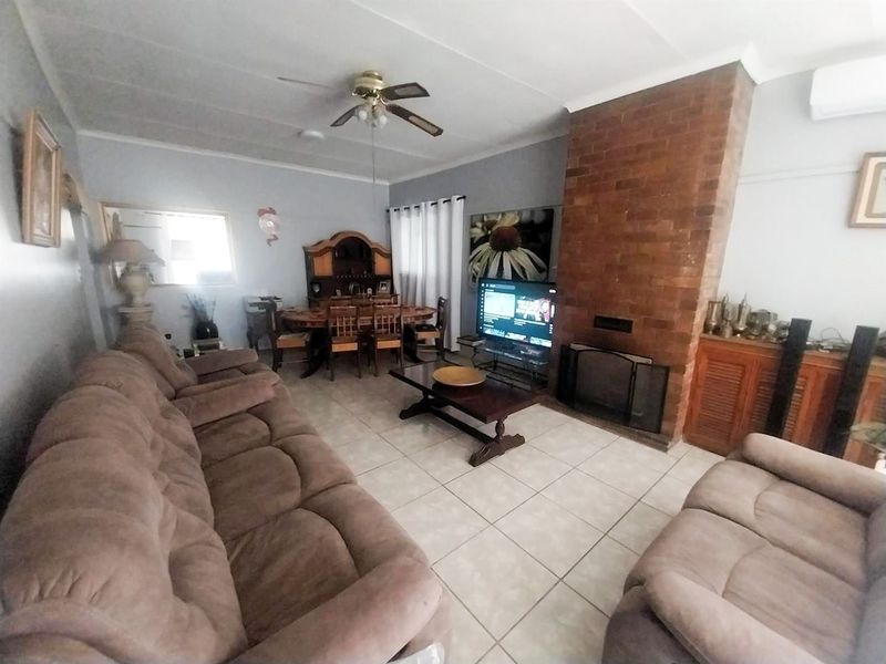 Spacious living room featuring a prominent brick fireplace, tiled flooring, and a ceiling fan, offering a comfortable and functional family space.