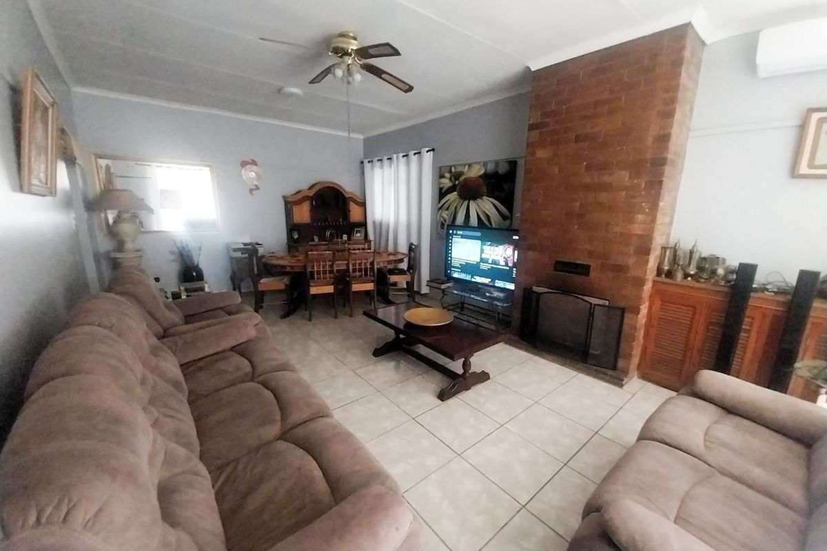 Spacious living room featuring a prominent brick fireplace, tiled flooring, and a ceiling fan, offering a comfortable and functional family space.