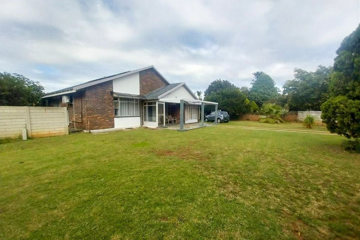 Rear view of a brick house featuring a covered patio area and a spacious garden with perimeter boundary walls.