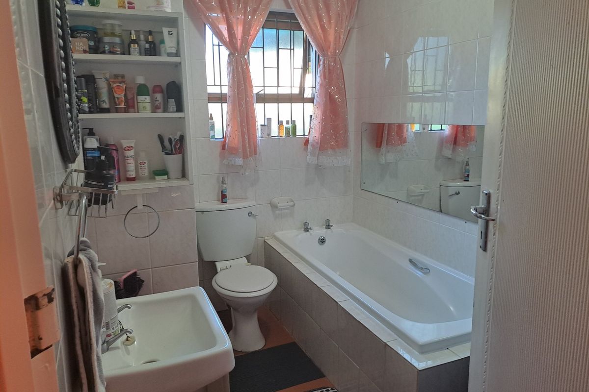 A functional bathroom featuring a built-in bathtub, pedestal sink, toilet, and integrated wall shelving with tiled walls.