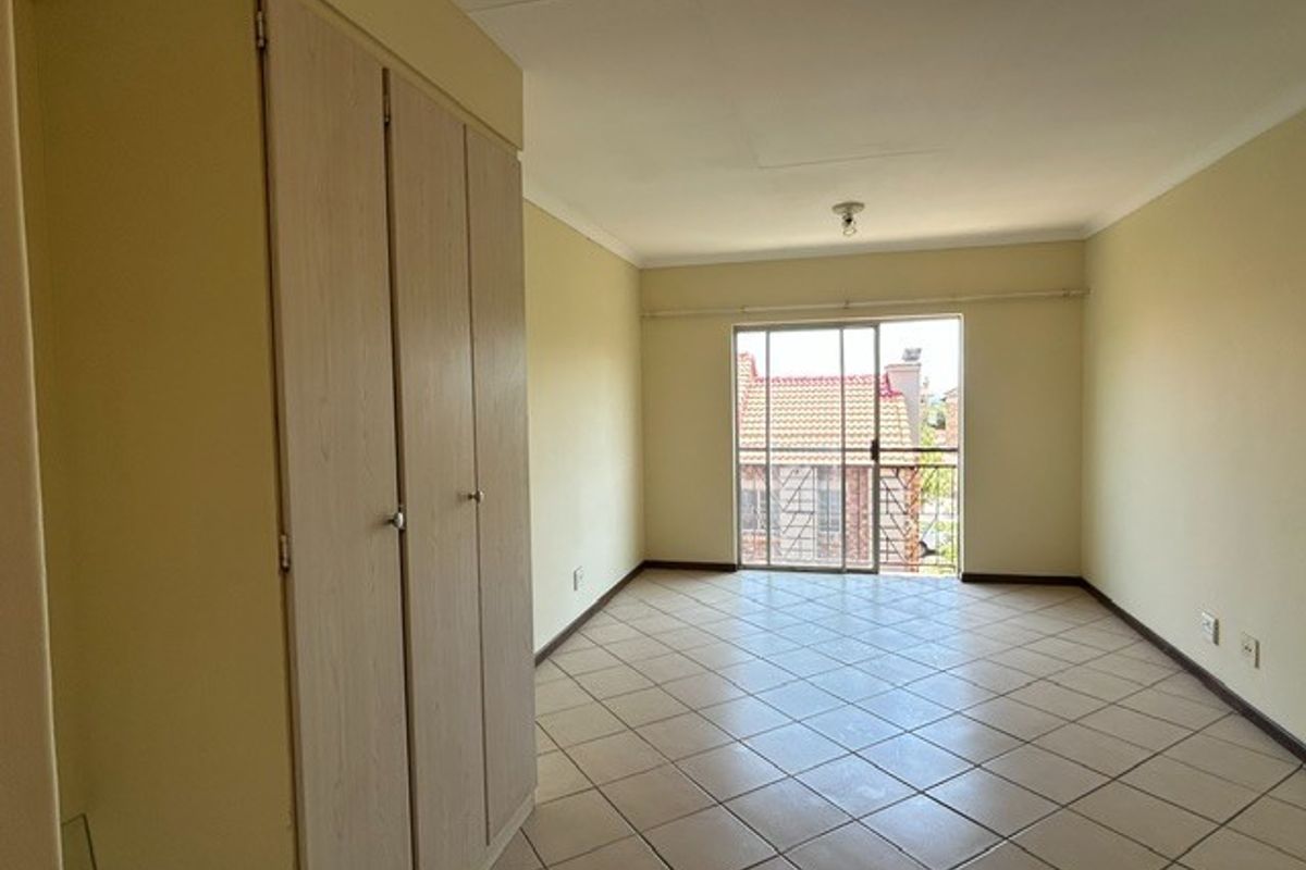 An empty bedroom featuring built-in cupboards, tiled flooring, and a sliding glass door providing access to a balcony.