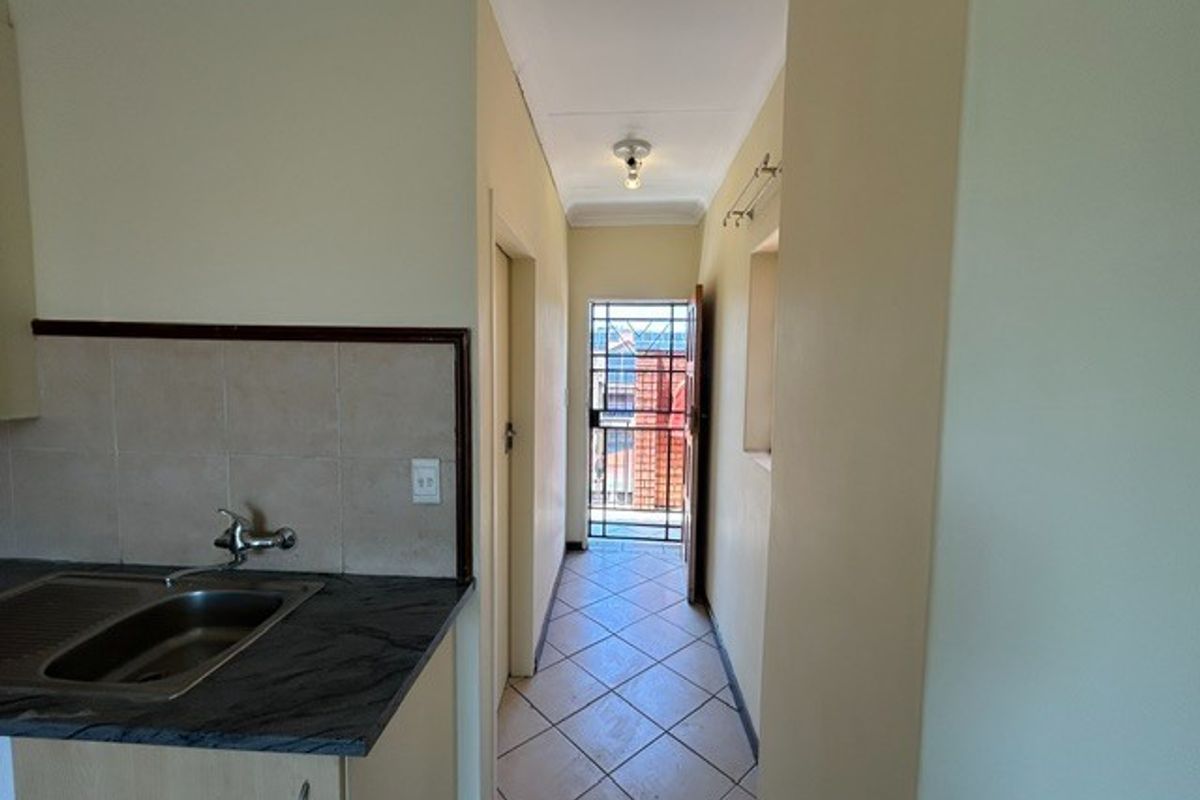 A functional kitchen area featuring a stainless steel sink, tiled backsplash, and direct access to an exterior security gate.