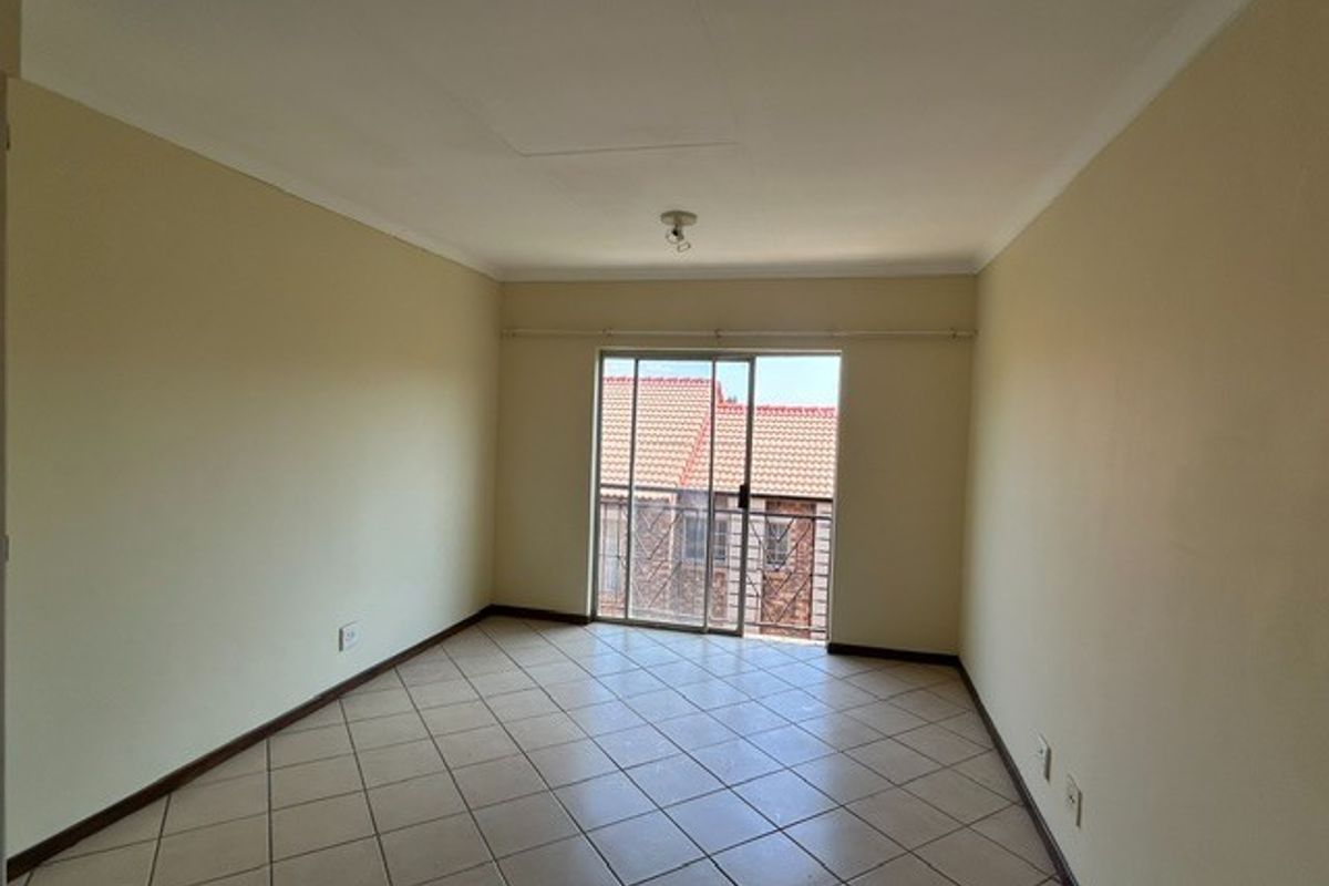 An empty living room featuring ceramic floor tiles, neutral walls, and a sliding glass door providing access to a balcony.