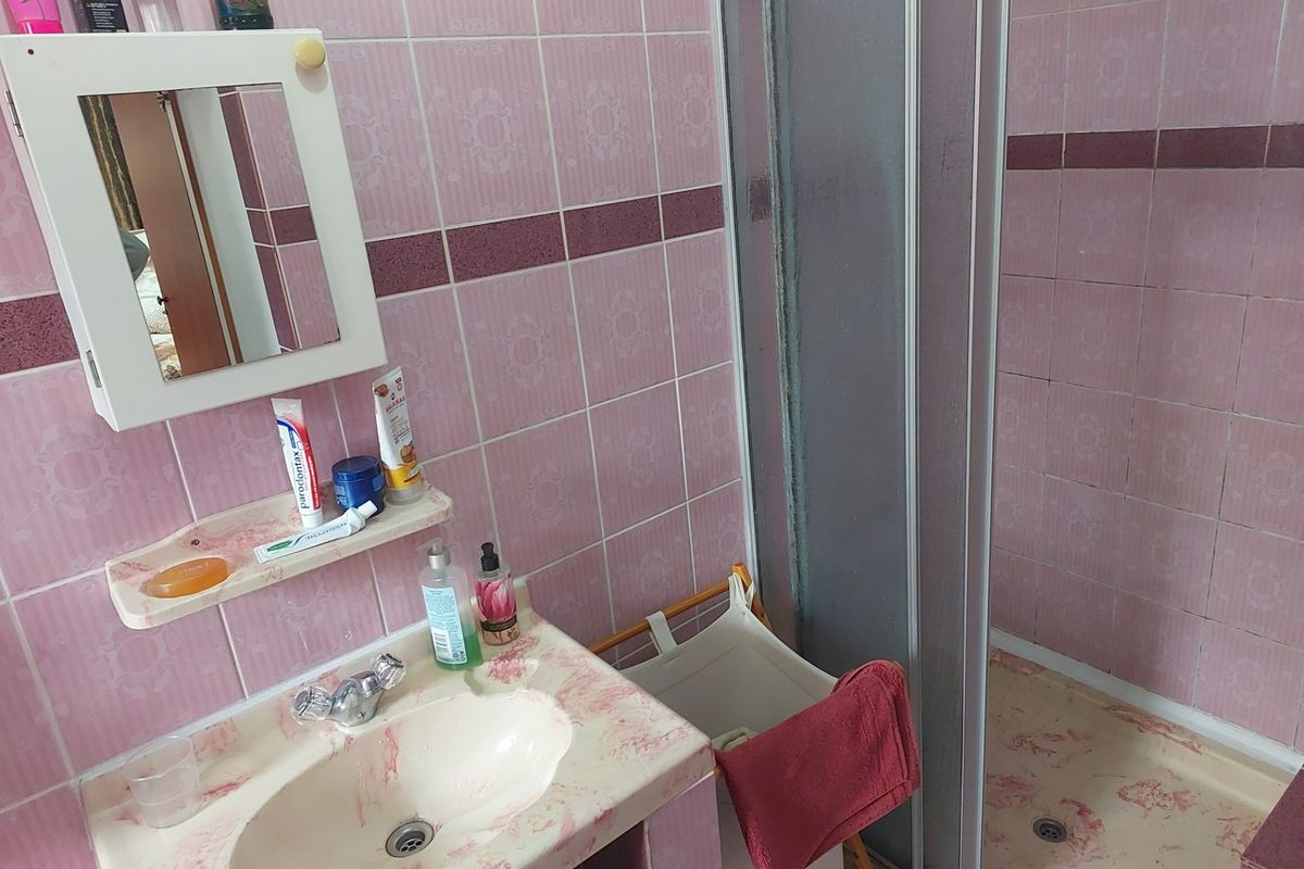 A dated bathroom featuring pink patterned wall tiles, a matching vanity basin, and a corner shower enclosure.