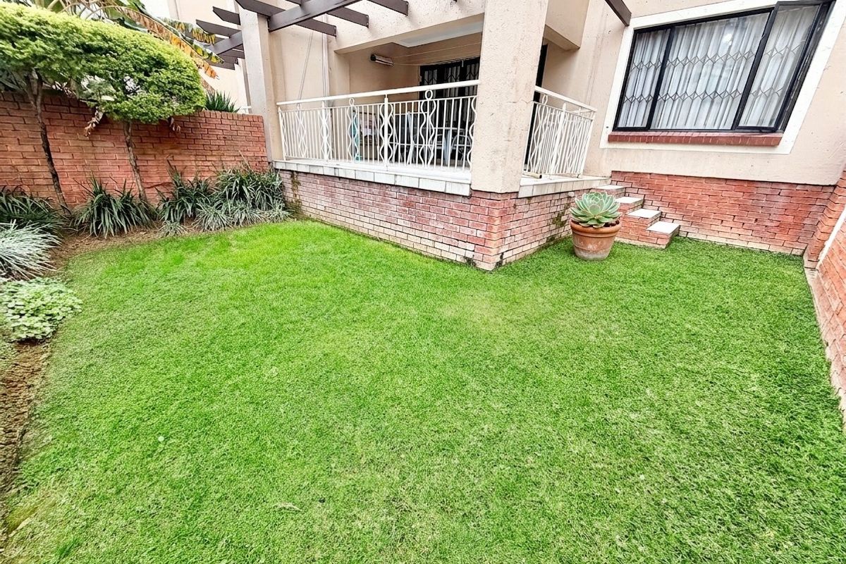 A private rear garden featuring a lawn area, a raised patio with a pergola, and secure metal balustrading.