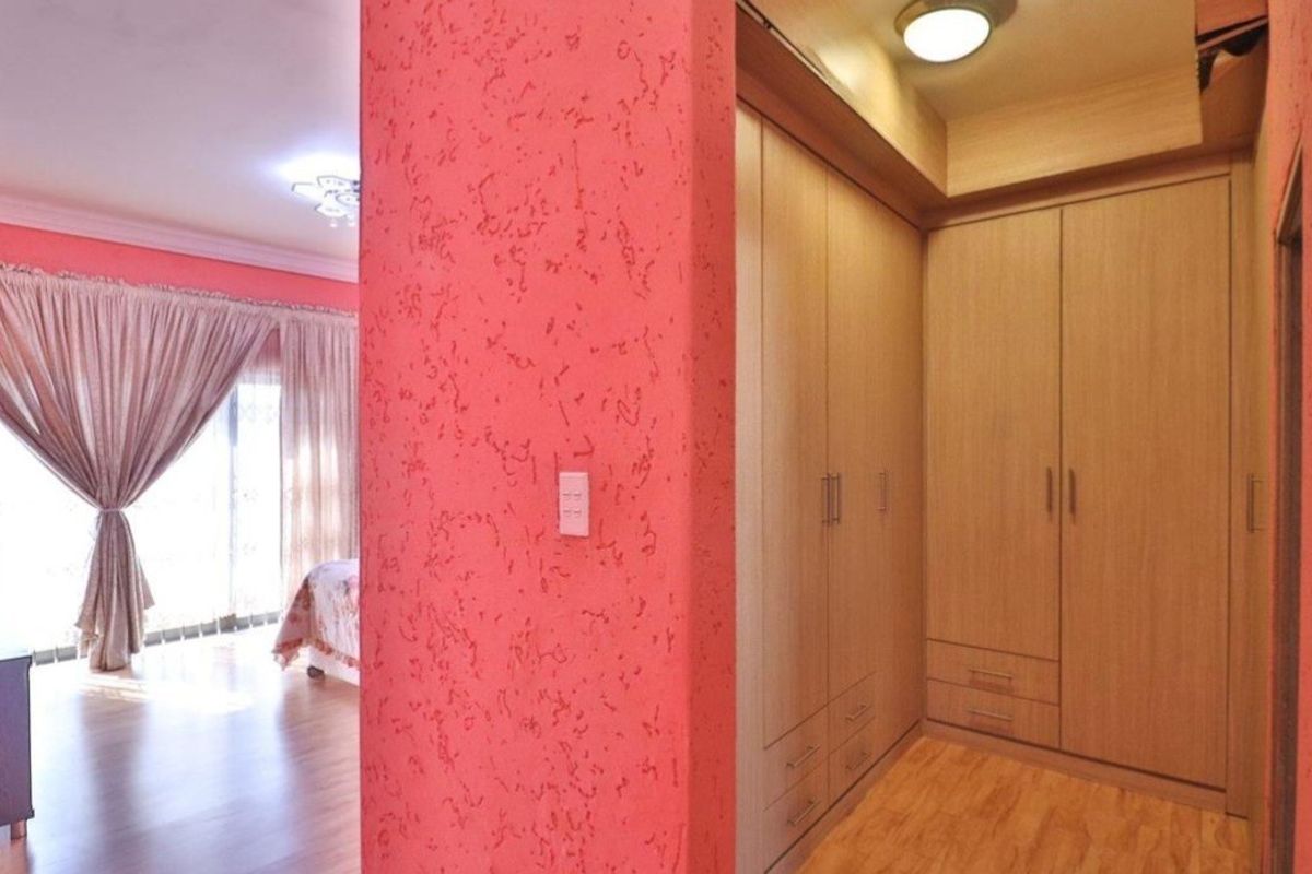 A bedroom featuring built-in wooden cabinetry and a textured accent wall, with an adjacent living area visible through the doorway.