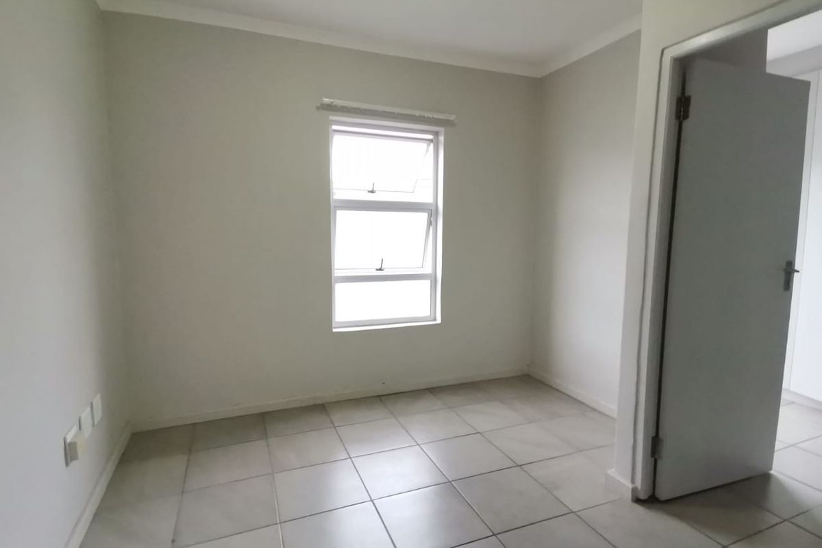 A bright, empty bedroom featuring neutral wall paint, tiled flooring, and a window providing natural light.