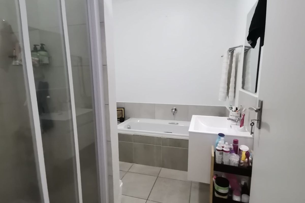 A functional bathroom featuring a built-in bathtub, a separate glass-enclosed shower, and a modern wall-mounted vanity basin with neutral floor and wall tiling.