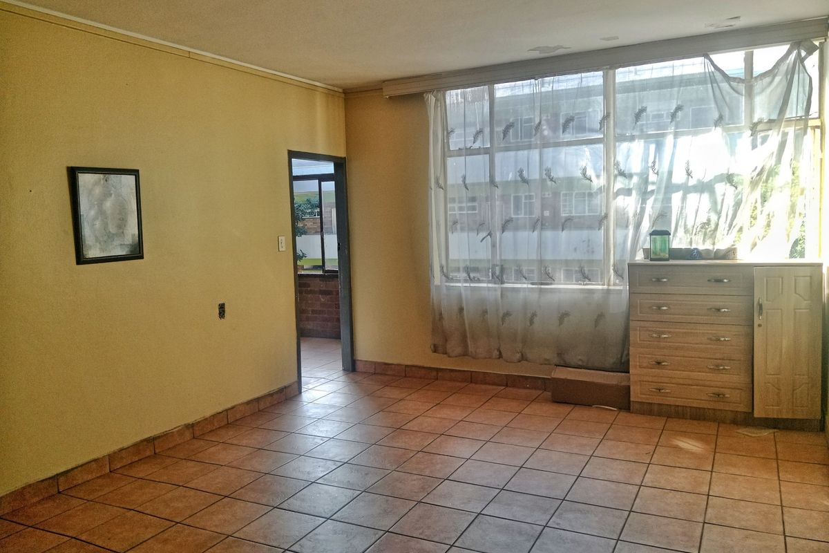 A spacious living area featuring large windows, tiled flooring, and neutral wall tones, offering a blank canvas for potential interior updates.