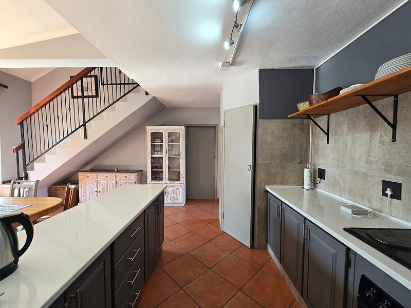 Open-plan kitchen featuring modern grey cabinetry, stone countertops, and a breakfast island, seamlessly flowing into the dining area with staircase access.