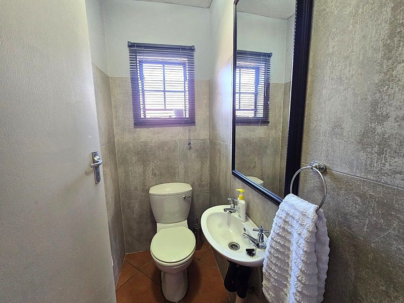 A compact guest bathroom featuring neutral wall tiling, a pedestal basin, a wall-mounted mirror, and a standard toilet.