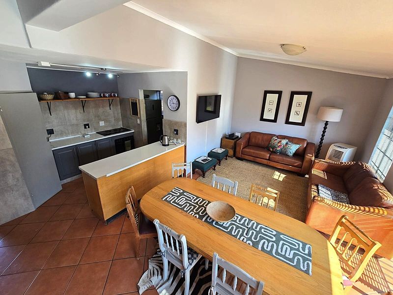 An open-plan living area featuring a kitchen with dark cabinetry, a dining space, and a comfortable lounge area with tiled flooring throughout.