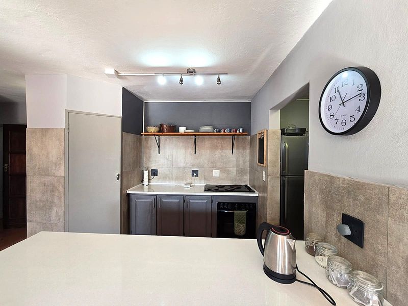 Compact kitchen featuring dark cabinetry, a built-in oven and hob, stone-look wall tiling, and a functional breakfast bar counter.