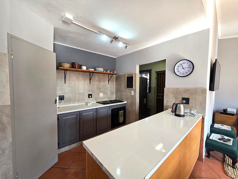 A modern kitchen featuring a breakfast bar, built-in oven, hob, and open shelving, with tiled flooring and neutral wall finishes.