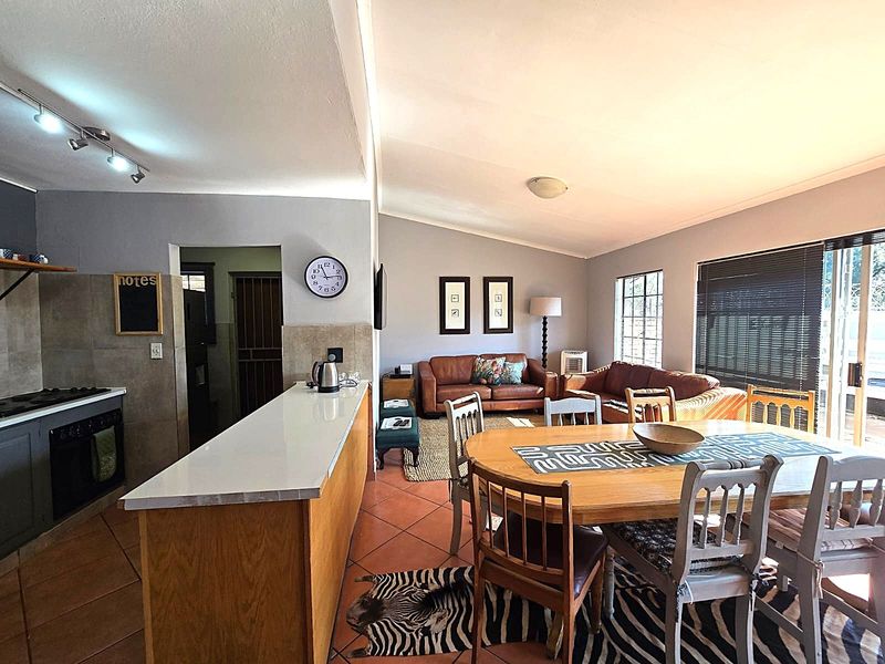Open-plan living area featuring a kitchen with breakfast bar, dining space, and lounge, characterized by tiled flooring and neutral wall tones.