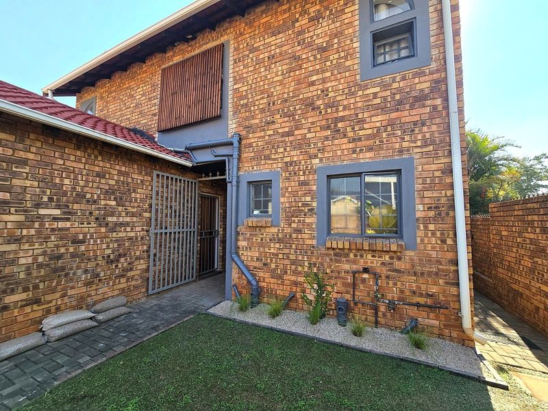 A view of the rear exterior of the house featuring face-brick walls, a paved walkway, and a small landscaped garden area.
