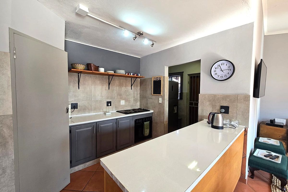 A modern kitchen featuring a breakfast bar, built-in oven, hob, and open shelving, with tiled flooring and neutral wall finishes.