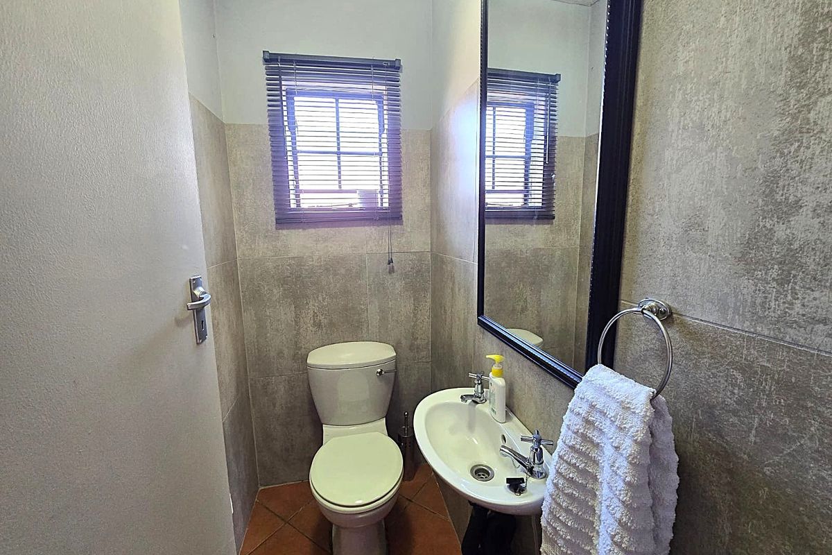 A compact guest bathroom featuring neutral wall tiling, a pedestal basin, a wall-mounted mirror, and a standard toilet.