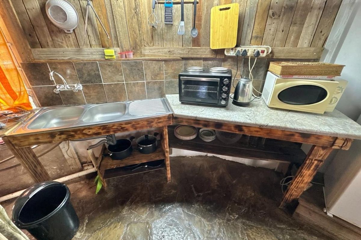 Rustic kitchen area featuring a stainless steel double sink, stone flooring, and timber wall paneling with open shelving storage.