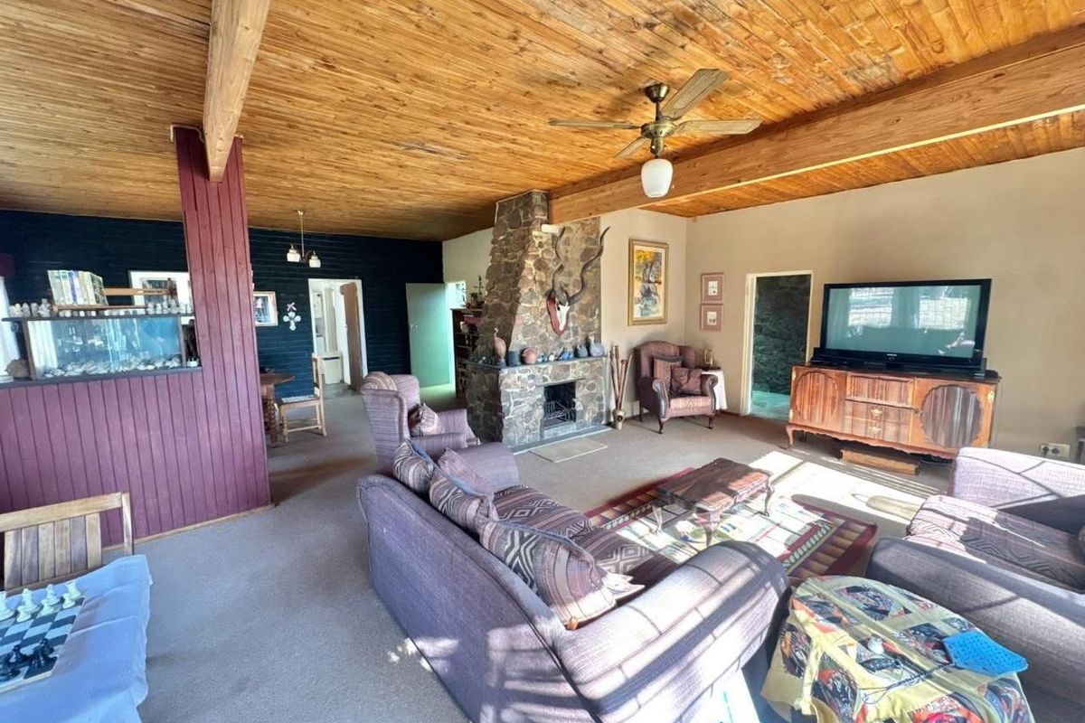 Spacious living area featuring a prominent stone fireplace, exposed timber beam ceiling, and open-plan layout connecting to adjacent rooms.