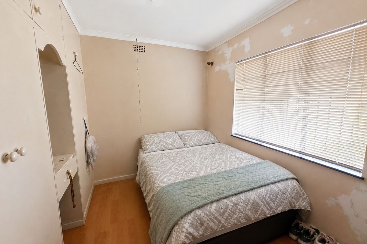 A compact bedroom featuring built-in cabinetry, laminate flooring, and venetian blinds, currently requiring cosmetic wall repairs and repainting.