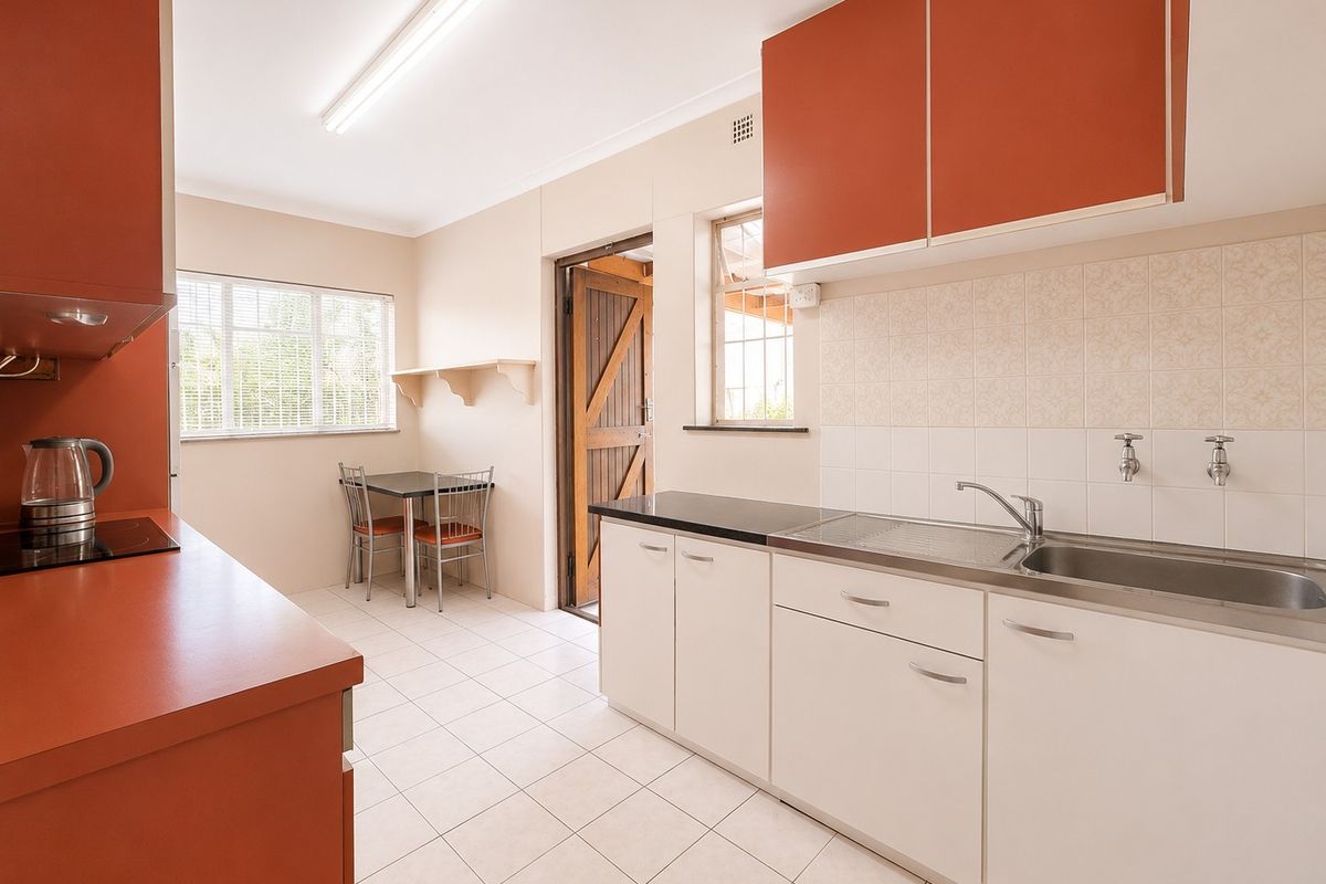 A functional kitchen featuring contrasting orange and white cabinetry, stainless steel sink, tiled splashback, and tiled flooring with direct access to the exterior.